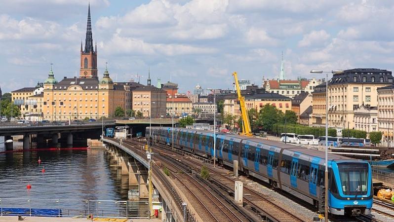 Vy över bron från Slussen mot Gamla stan med ett tunnelbanetåg. I bakgrunden syns Riddarholmskyrkans spira.