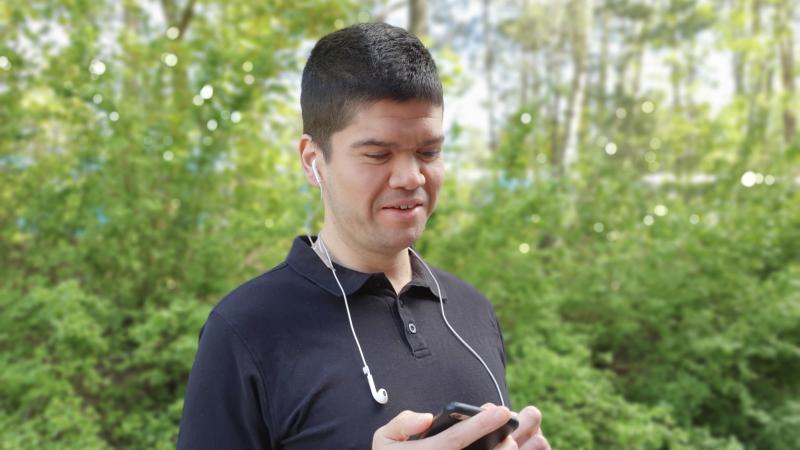 Man i närbild med kort mörkt hår tittar ner på sin mobil, står i skogen