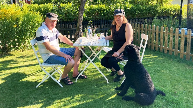 Kvinna och man sitter vid bord i en solig sommar trädgård