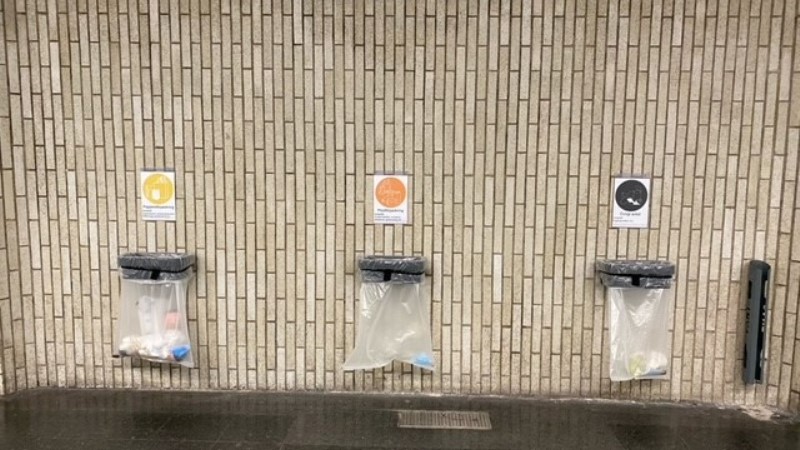Tre papperskorgar bredvid varann, hänger på vägg, tunnelbanestation.
