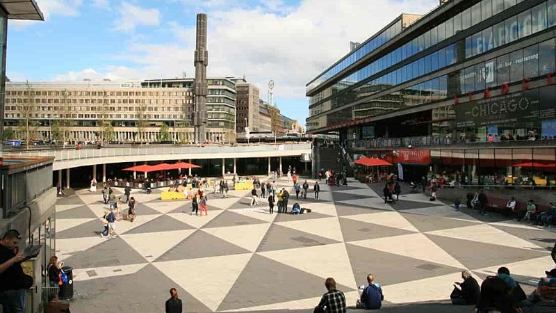 Sergels Torg sett från trapporna vid Drottninggatan. Några människor är utspridda, i bakgrunden syns pelaren i fontänen vid rondellen.