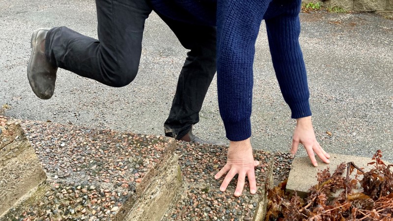 Närbild person som faller och tar emot sig på stentrappa. Har mörka jeans och mörkblå tröja.