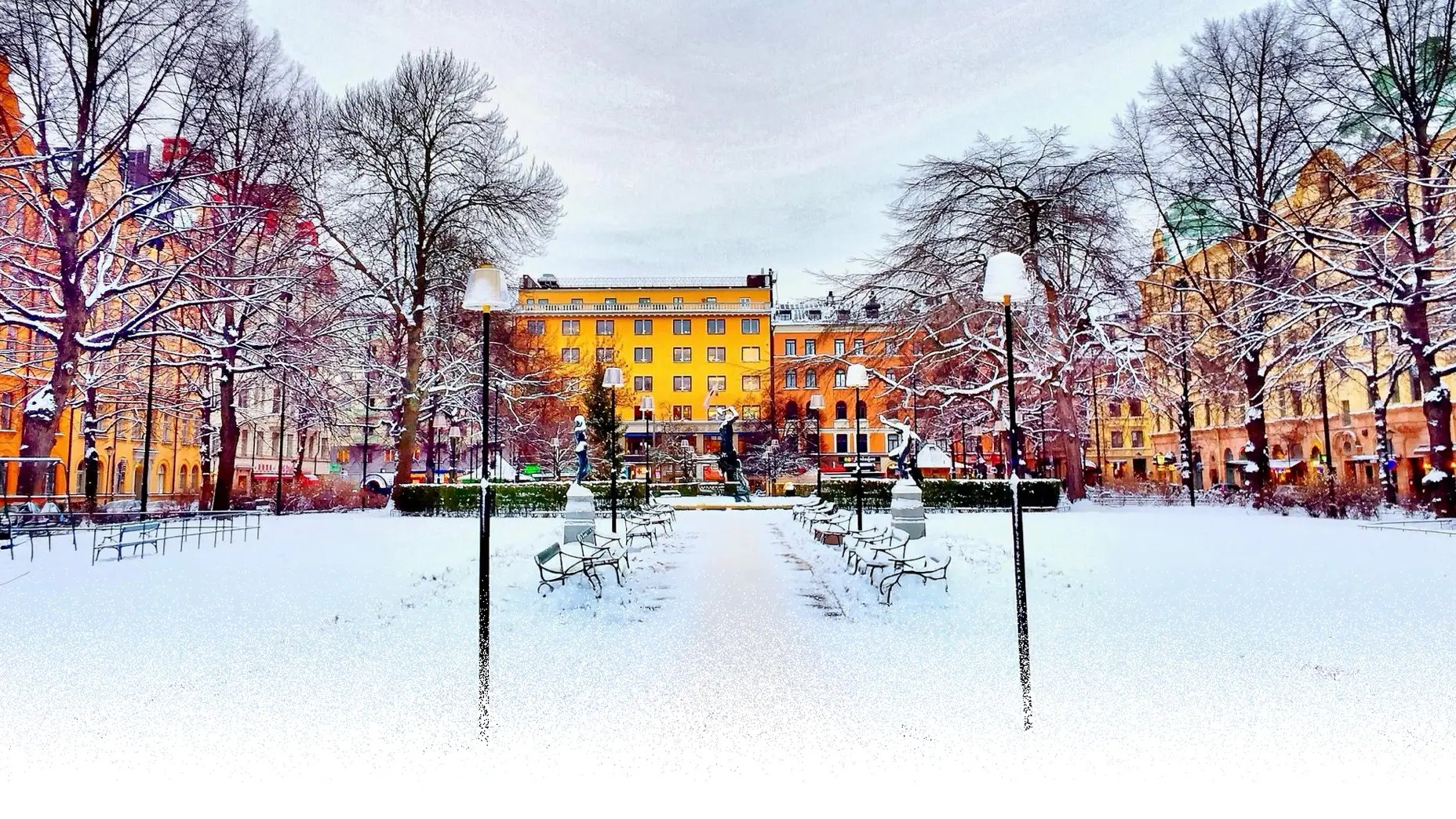Foto på snöklädd park kantad av stadshus och trädallé.