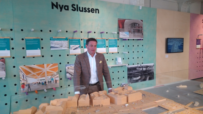 Man i grå kavaj står framför en modell av Slussenbygget.