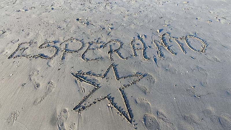 En sandstrand där någon skrivit ordet ESPERANTO i sanden och ritat en femuddig stjärna under.
