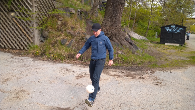 Man i blå träningsjacka med byxor sparkar en fotboll