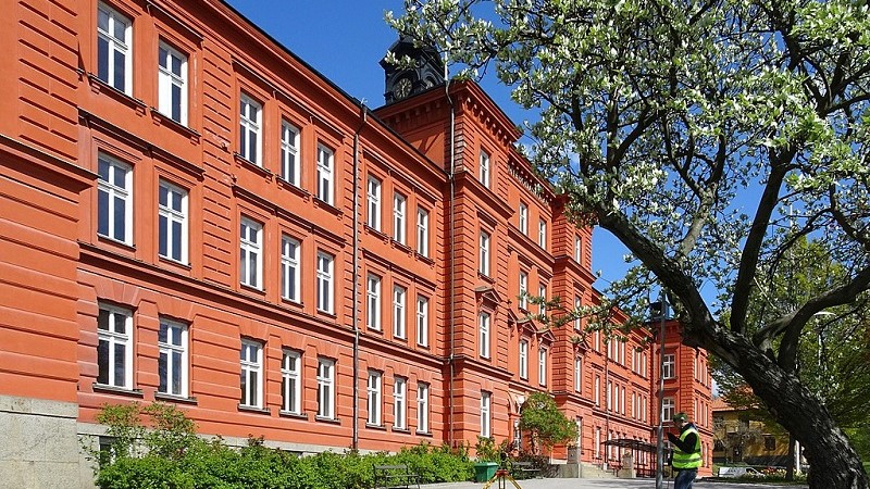 Tomteboskolans fasad i rödbrun puts. Framför skolan står ett träd i blom.