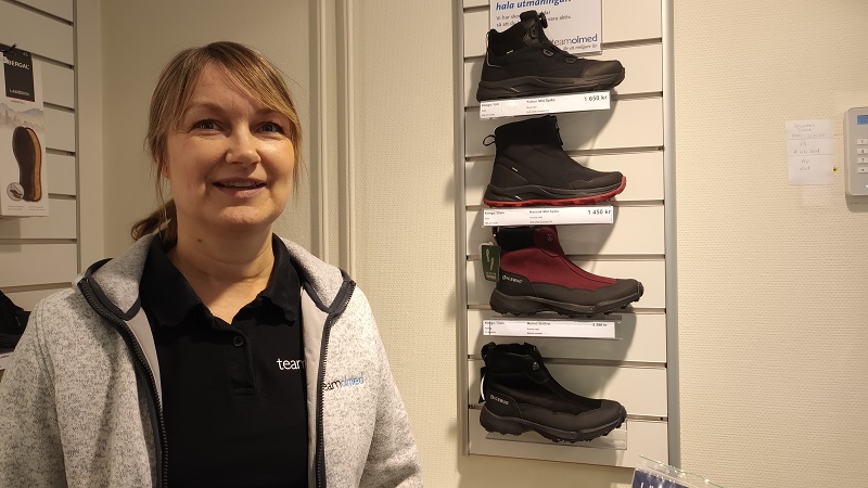 En blond kvinna med glasögon och halvlångt hår står framför en hylla med några olika skor med extra bra grepp.