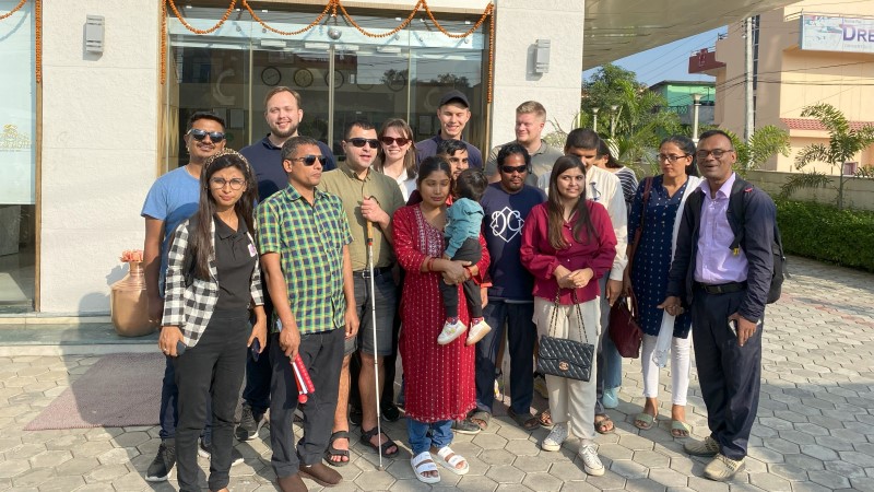 Flera yngre personer står bredvid varandra utanför vit byggnad i Nepal.