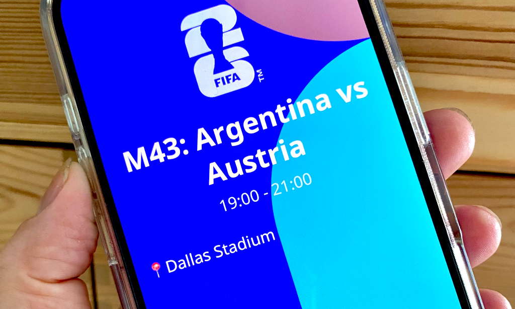 En ljushyllt hand håller i en mobil. På skärmen en blå, grön mönstrad bakgrund med vit text: Fifa. Argentina VS Austria 19:00-21:00