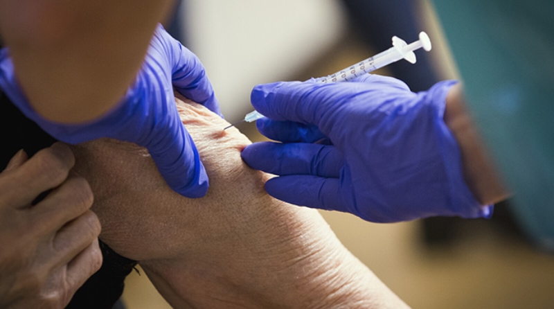 Hand med blå plasthandske, sätter spruta i arm
