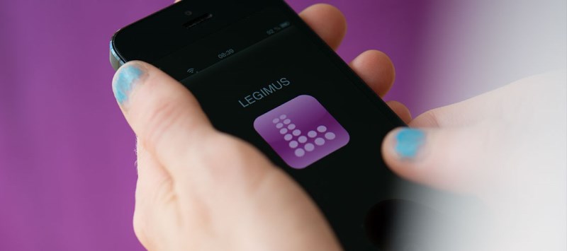 Hand håller i mobil, legimusapp syns, bakgrund lila vägg