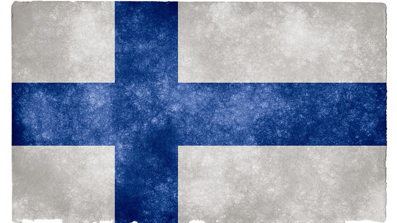 En konstnärlig bild av en finsk flagga, lite fläckvis genomskinlig och ojämn i kanterna. Mörkblått liggande kors på vit botten.