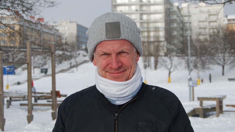 Man i snöigt landskap. Grå, stickad mössa, vit halsduk. 