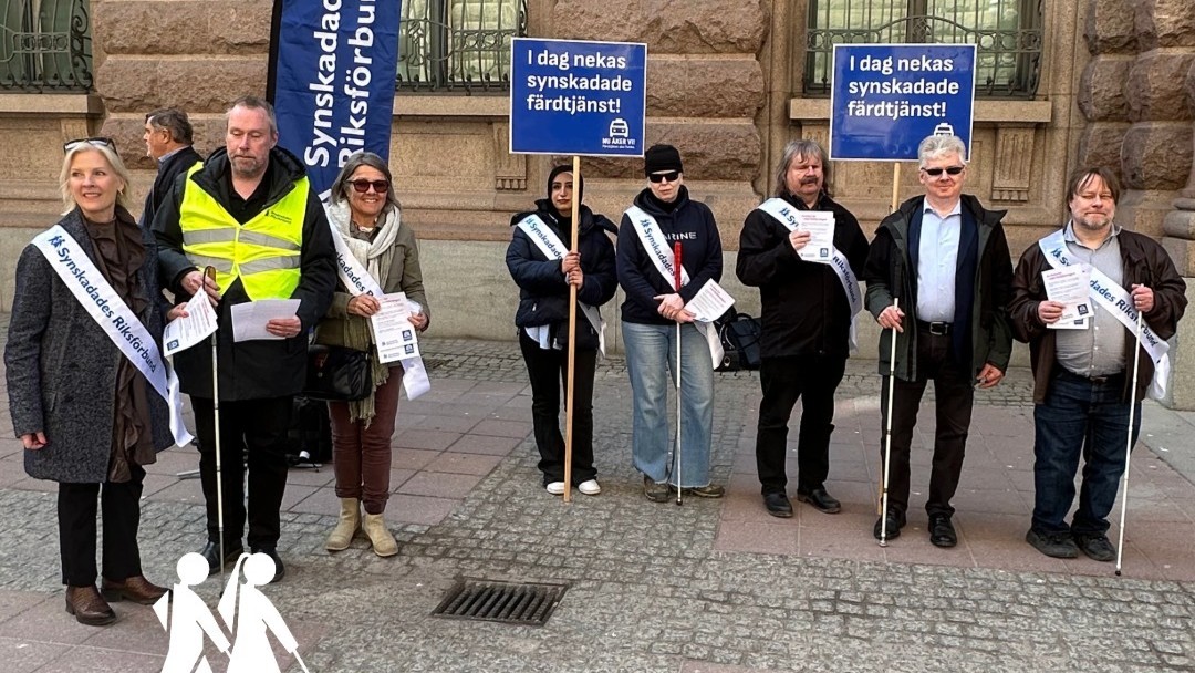 8 personer står med vita SRF ordensband och några med skyltar med text: Synskadade nekas färdtjänst