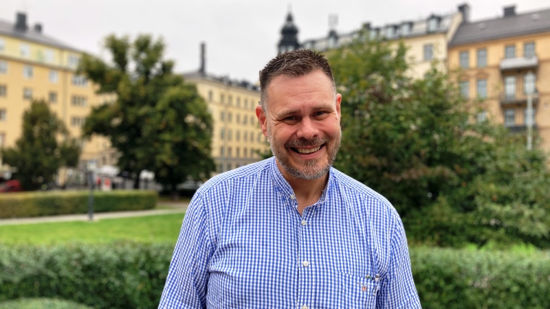 Leende kortklippt man i ljusblå skjorta står i grön park
