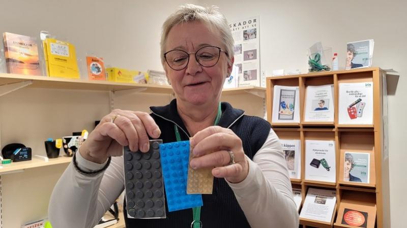 En vit kvinna med blont kortklippt hår och glasögon håller upp ark med gummipluppar i olika storlek och färg.