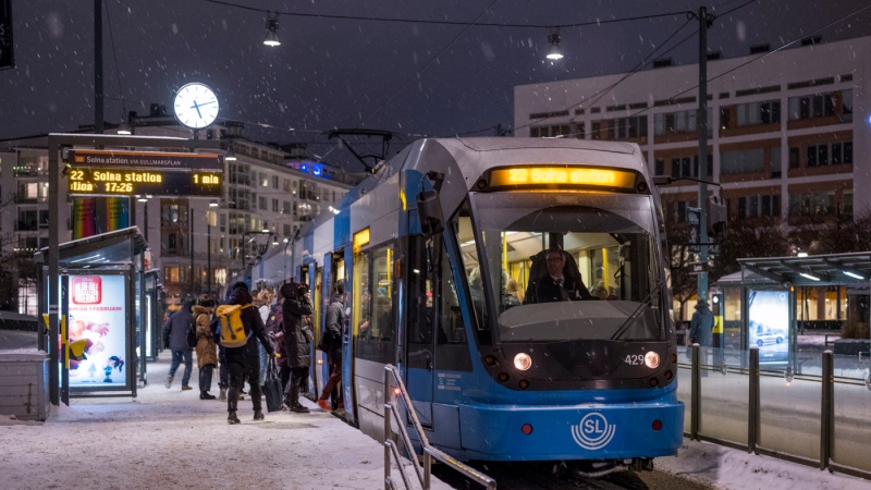 Blå tvärbanetåg står på plattform. Kväll, snö.