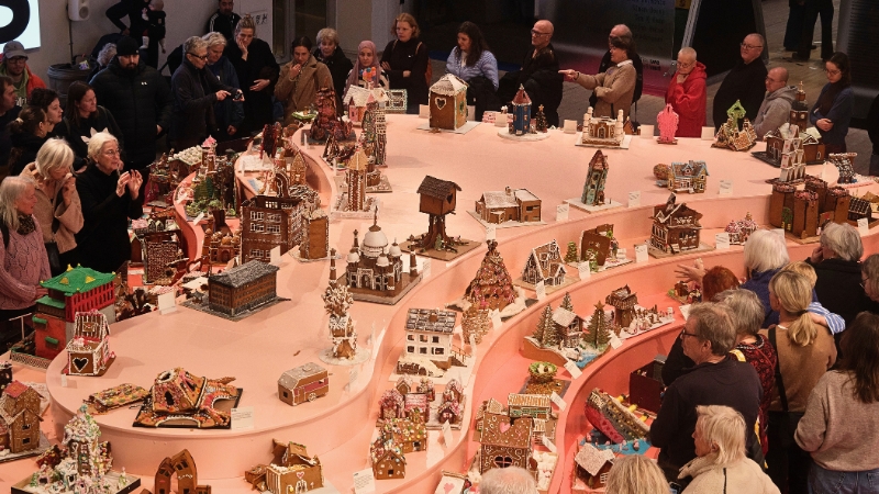 En översiksbild tagen från avstånd där man ser ett svängt rosa podium i tre etager fylld med pepparkakshus i fantasifulla former. Runt podiet står människor och tittar och pekar. 