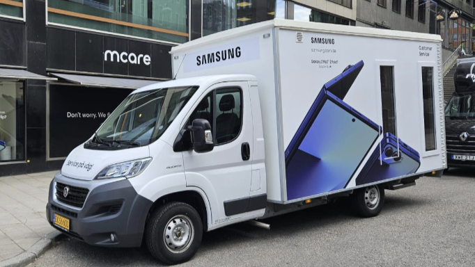 En vit lastbil står parkerad på en gata i Stockholms city. Bilen har dekor av 2 stora foton av mobiltelefoner.