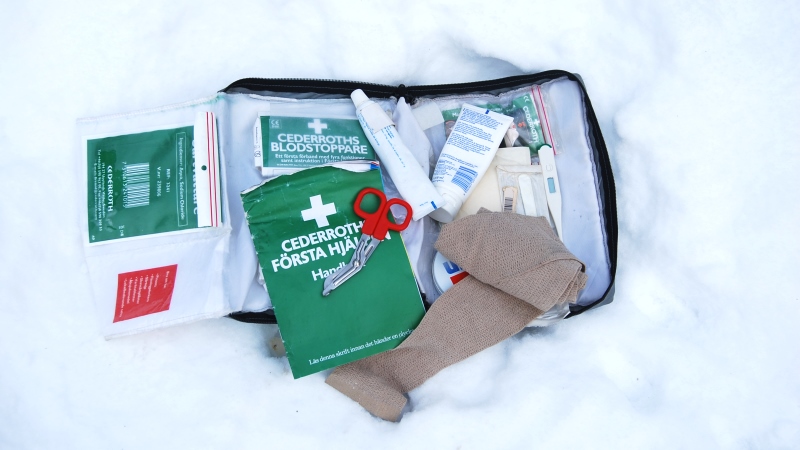 Första Hjälpen väska ligger uppslagen i snön, med diverse plåster och kompresser.