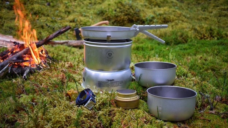 Ett stormkök, aluminiumkastrull över gaslåga. Grön mark.