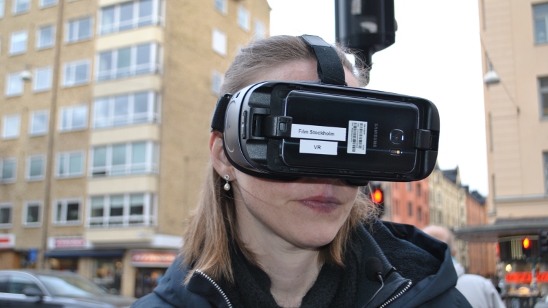 Rödblond kvinna i närbild, hon har på sig ett par VR glasögon, stadsbild.