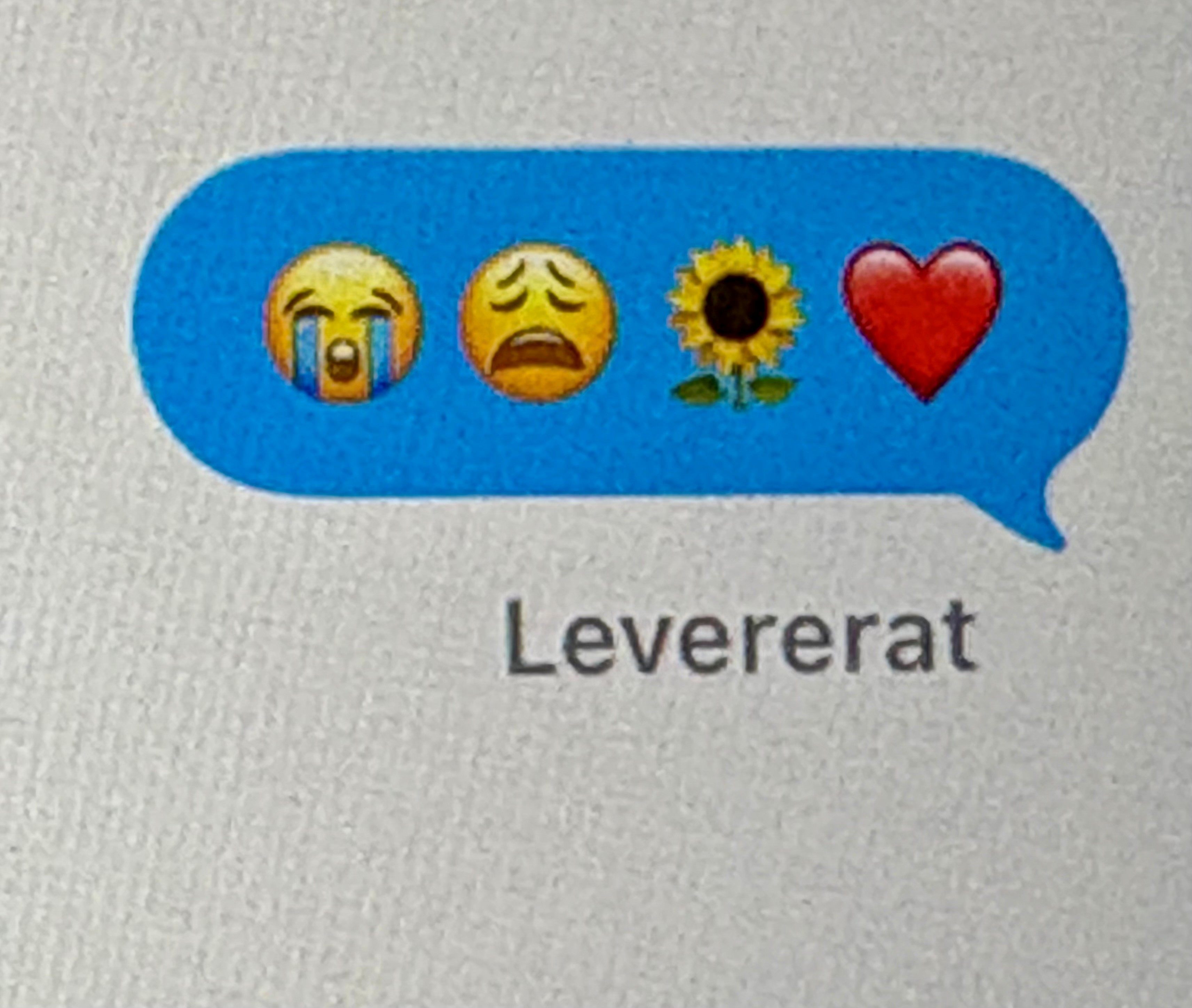Bild från mobil av några emojis. Storgråtande emoji, en med ledsen mun, en gul solros, och ett rött hjärta. De är alla i en blå smspratbubbla.