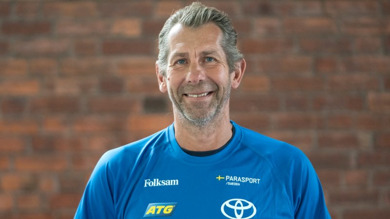 Leende vit medelålders man med bakåtkammat grått hår och skäggstubb, har blå T-tröja. Står mot röd tegelvägg.