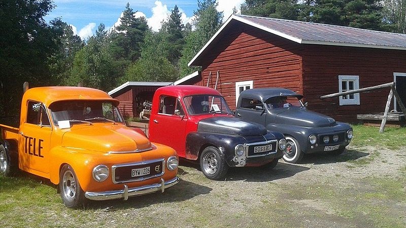 Tre EPA-traktorer med lång front parkerade på en gårdsplan bredvid varandra, en brandgul, en röd med svart huv och en helsvart. I bakgrunden en faluröd timrad lada.
