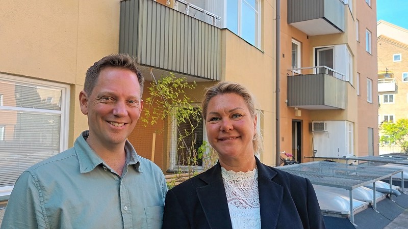En blond man och en mörkblond kvinna står på en innergård framför en fasad i sandstensputs. 
