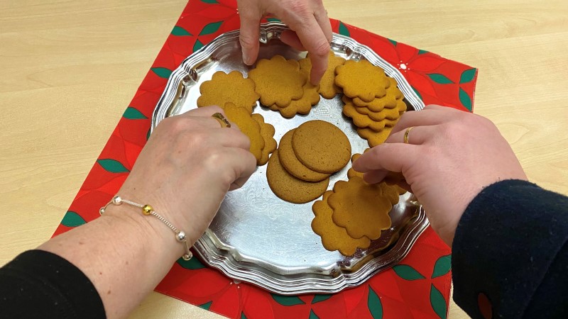 Några händer sträcker sig över flera bruna pepparkakor på ett silverfat.