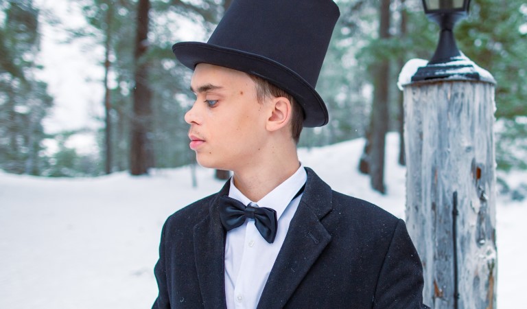 Ung vit kille, med  kavaj, fluga, hög cylinderhatt i svart. Står i vintrig skog