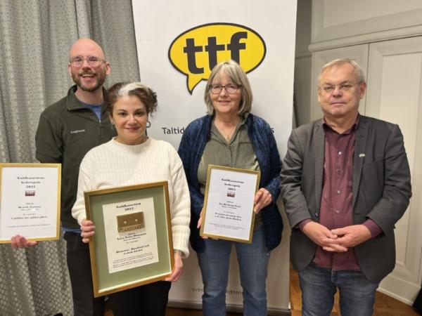 Fyra personer på rad framför en banderoll med texten "ttf" i en gul pratbubbla. Tre av personerna håller tavlor med prisplaketter. Personerna är från vänster Henrik Jansson, Aziza Dhaouadi, Åsa Kjellman Erici och Bert Sundström.