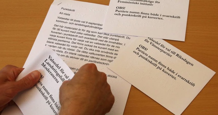 På ett bord ligger flera valsedlar på punkt. Två händer läser texten.