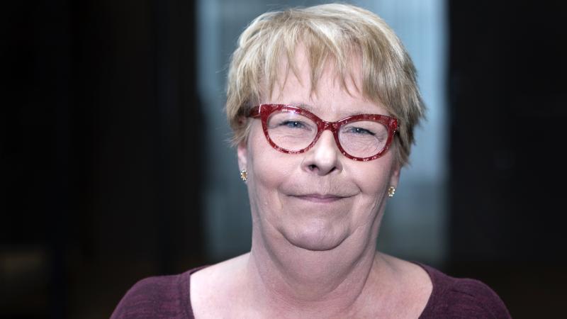 Leende kortklippt kvinna med blondrufsig frisyr i lugg och med röda glasögon.
