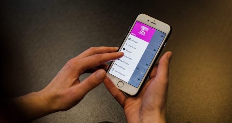 Två händer håller i en mobiltelefon där appen Legimus visas på skärmen.