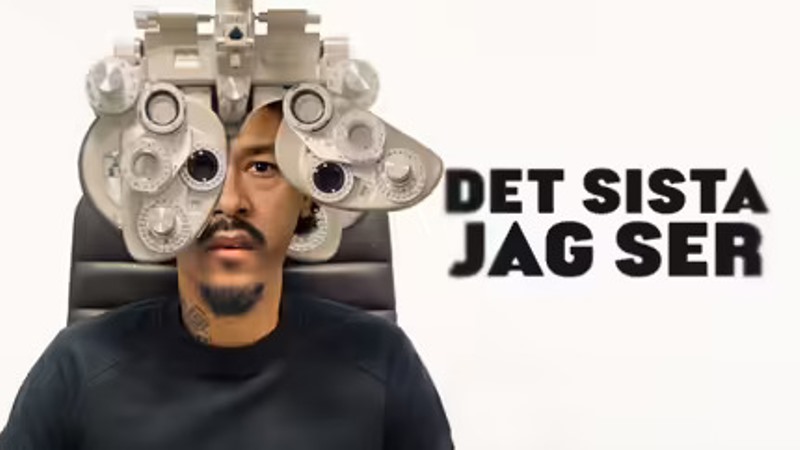En svart 30-årig man med svart mustasch och skägg, ser in i en ögonmätningsapparat hos optiker.