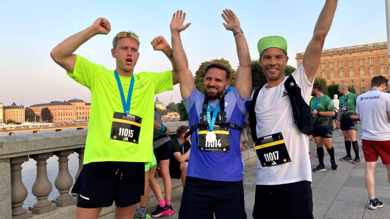 Tre vita män i trettioårsåldern står bredvid varandra med händerna uppsträckta över huvudet i segergest. Träningskläder, nummerlappar och medalj på. Bakgrund Stockholms slott. 