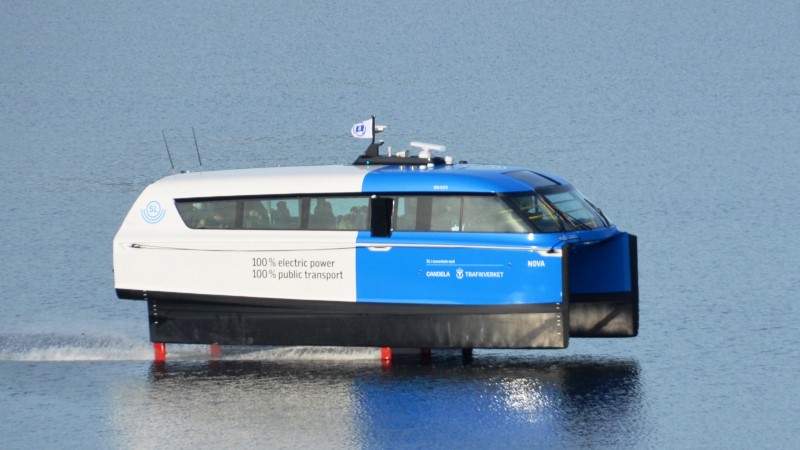 En blåvit bärplansbåt i SL trafik, som ser ut att sväva ovanför vattenytan, åker på gråblått vatten. 