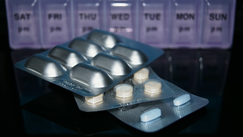 Tre ark med olika mediciner ligger på ett bord framför en dosett med veckodagarnas namn på engelska.