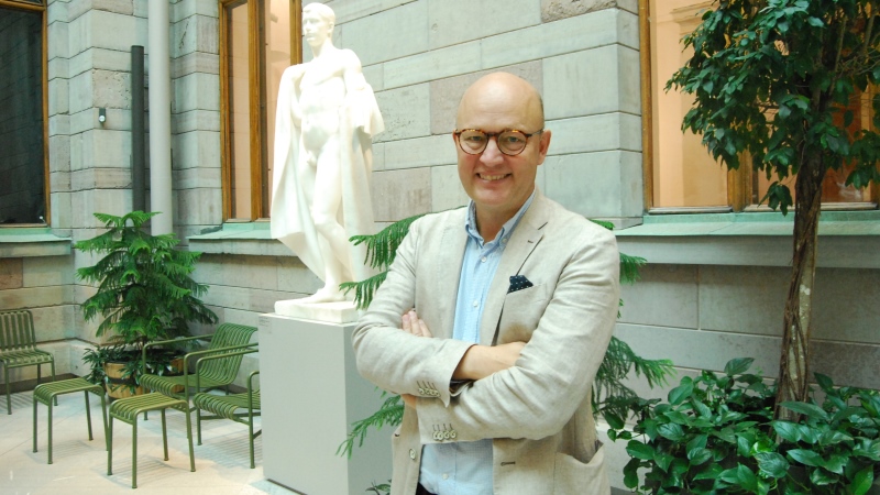 Skallig man med gula glasögon, i ljusblå skjorta och beige kavaj på museum