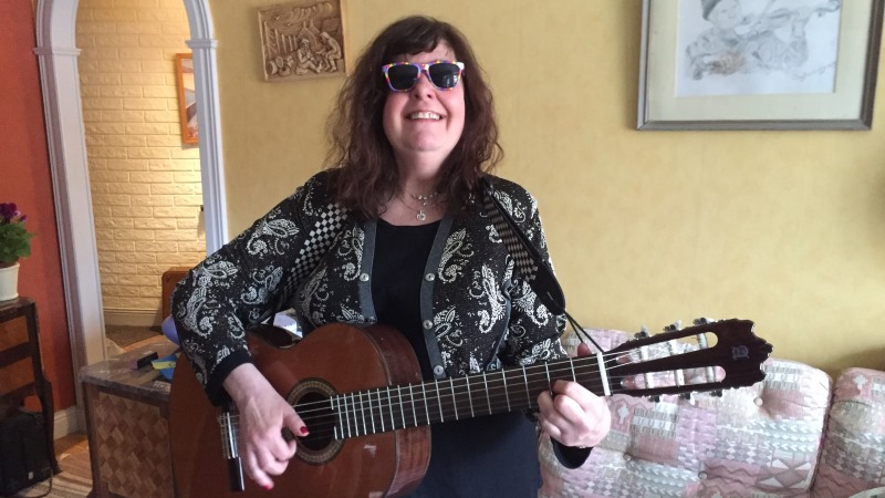 Brunhårig leende kvinna med gitarr i knät, sitter i en ljus soffa
