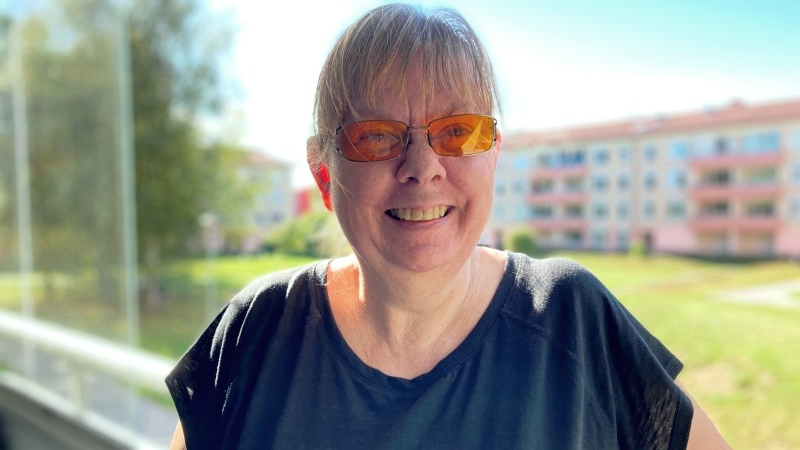 Leende kvinna i glasögon och tofs står på sin balkong
