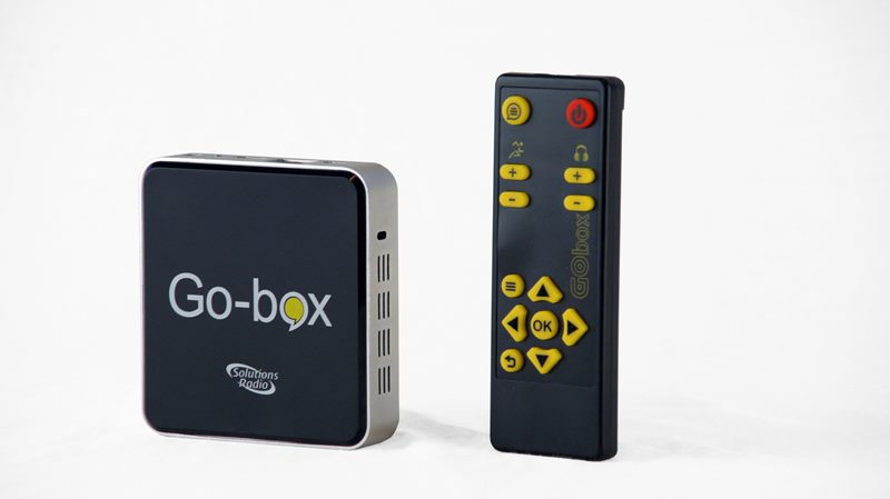 En fyrkantig svart digital box ( 10x10 cm) med vit text ”Go-box+” bredvid en svart fjärrkontroll med gula knappar.