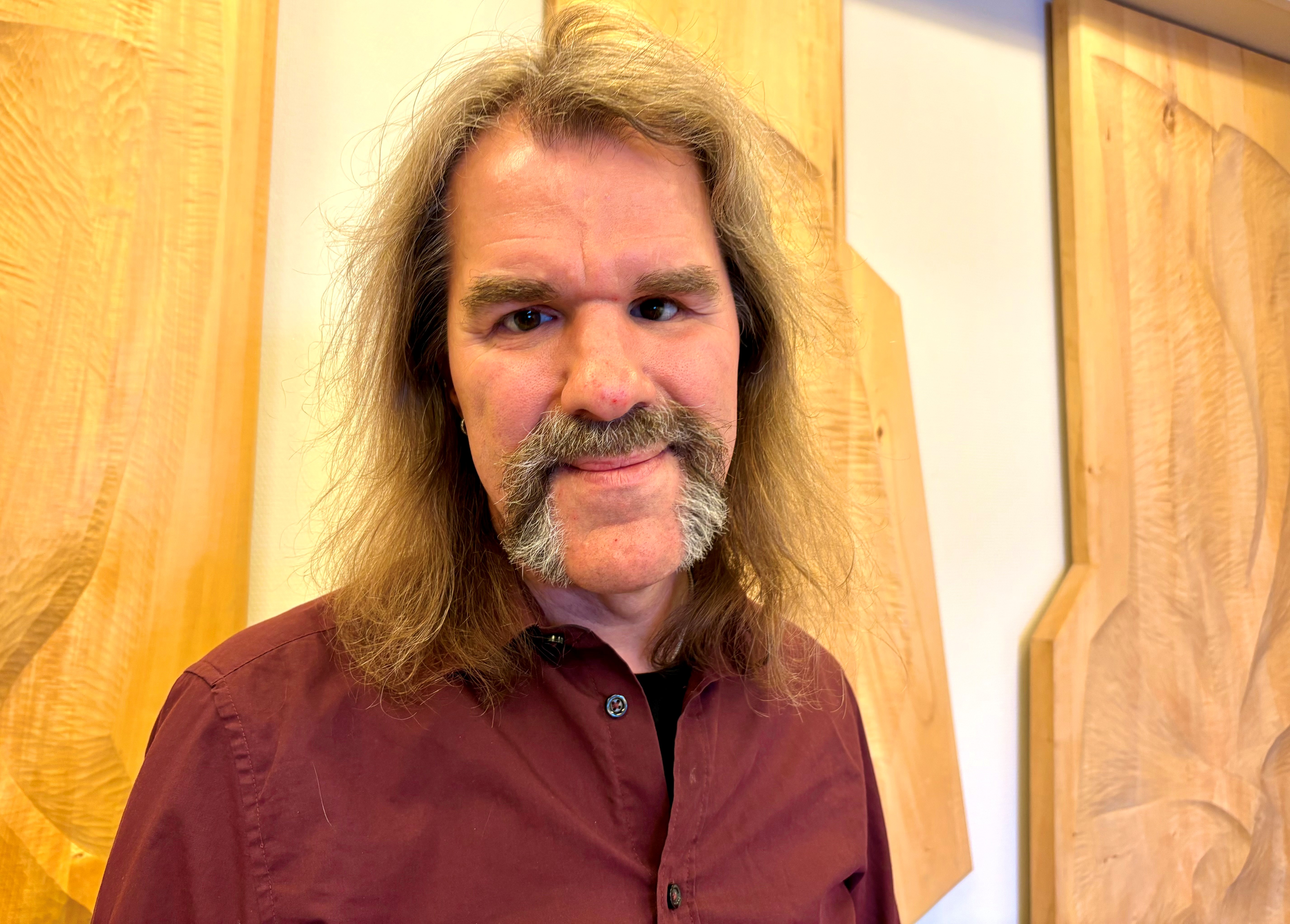 Vit medelåldersman med ljusbrunt axellångt hår, bruna ögon. Kraftig mustasch som går ner längs munnens sidor och går ihop med skägget, i avslutande breda strängar ned till hakan. Han har vinröd skjorta.