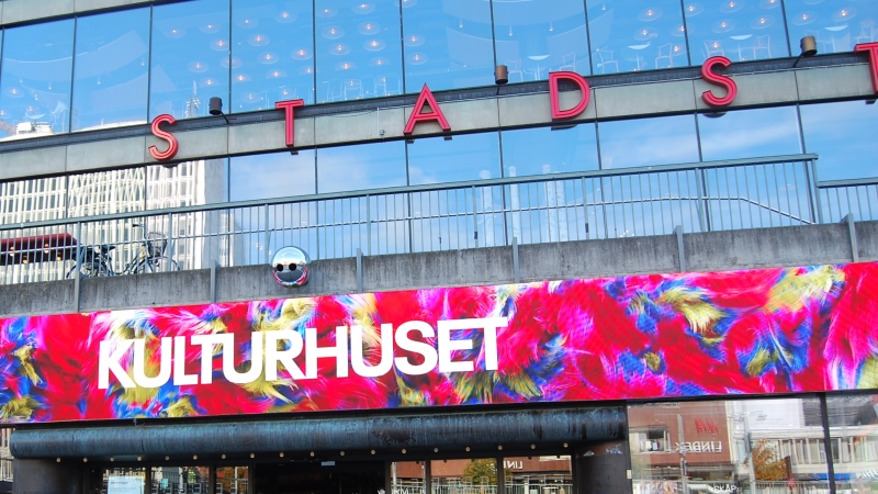 Skylt på glasfasad med vita versaler KULTURHUSET mot bakgrund av starka röda, blå och gula färger i abstrakt mönster.