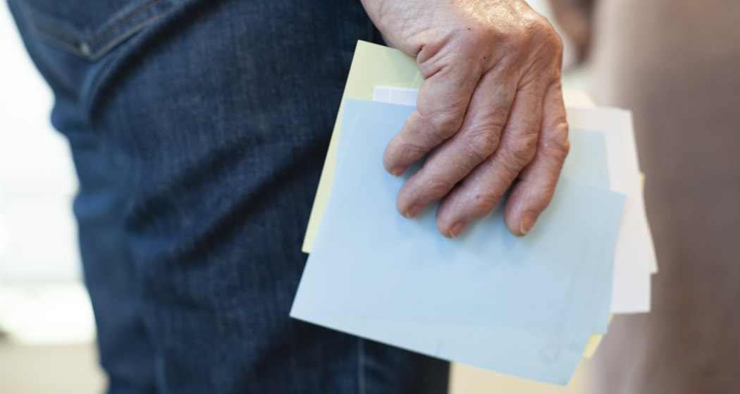 En närbild på en vit persons hand håller flera färgglada valsedlar i handen.