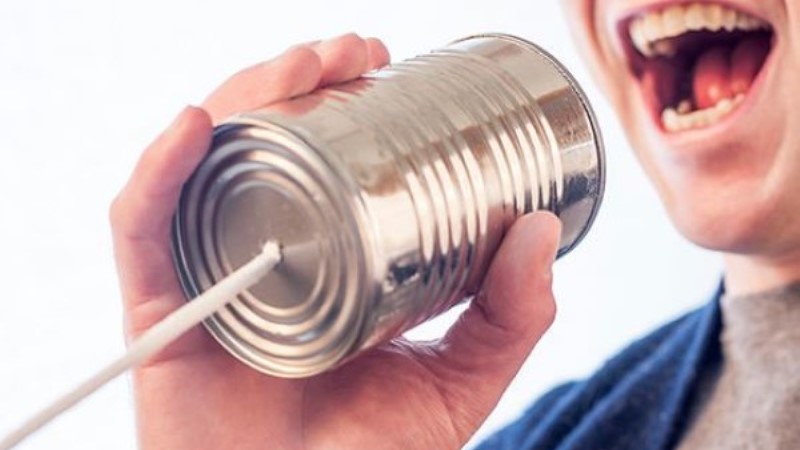 Ansikte i närbild, man pratar i en stålfärgad konservburk med tråd i botten, som en telefon.