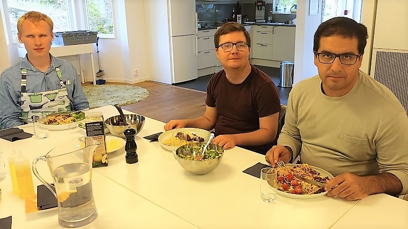 Tre unga män sitter vid ett matbord med tallrikar och pasta på. Till vänster en blond kille, Johannes, i mitten Elliot som är brunhårig och till höger Saman som är mörkhårig.